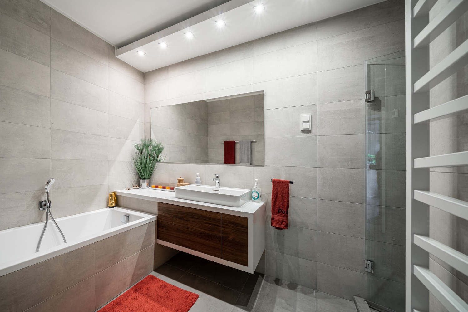A nagyobb fürdőszoba tökéletes komfortot kínál: kényelmes méretű káddal, könnyed mosdópulttal, fölötte hatalmas tükörrel, mindemellett még egy zuhanyfülke is elfért a helyisgében.