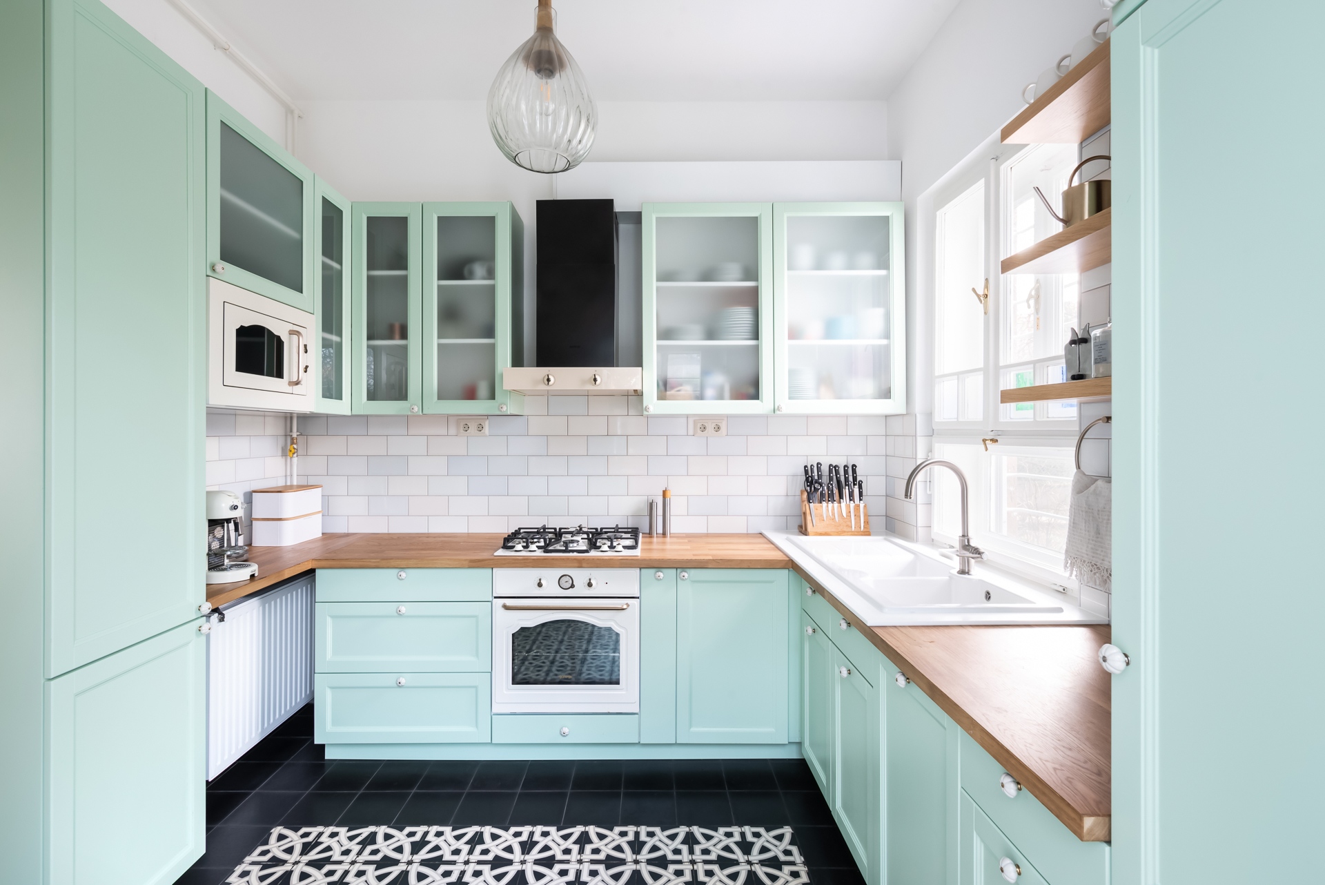 Az eredeti, megőrzött cementpadlóhoz üde zöldes színű, egyedi konyhabútor készült, amihez fehér, rusztikus stílusú konyhai gépeket választottak.