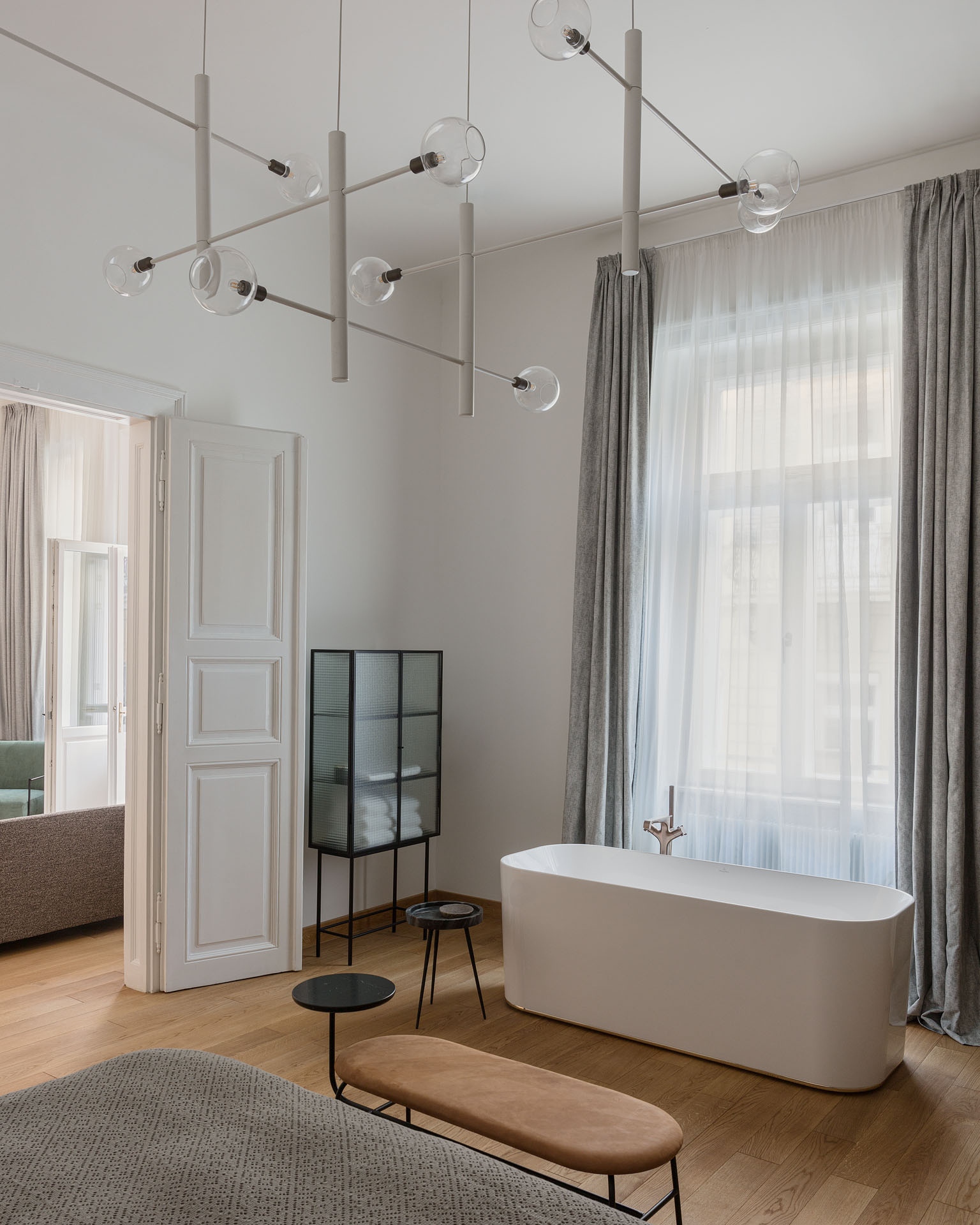 A nagyobbik háló attrakciója a térben álló fürdőkád, amelynek lekerekített formája az ágy végében álló filigrán ülőbútorral harmonizál. A felújított klasszikus ajtók hangsúlyos szerepet kapnak a modern, geometrikus bútorok között.