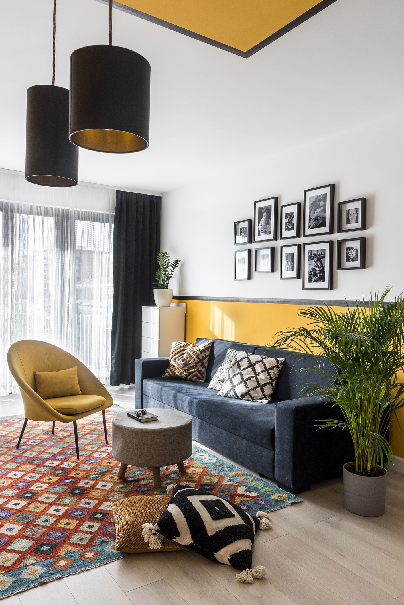  A tervezés kiindulópontját jelentő Kilim szőnyeg színes, geometrikus mintáihoz jól illenek a kanapé díszpárnái és az egyedi, sárga falburkolat, de a szintén egyedi tervezésű könyvszekrény is sajátos hangulatot kölcsönöz a nappalinak.