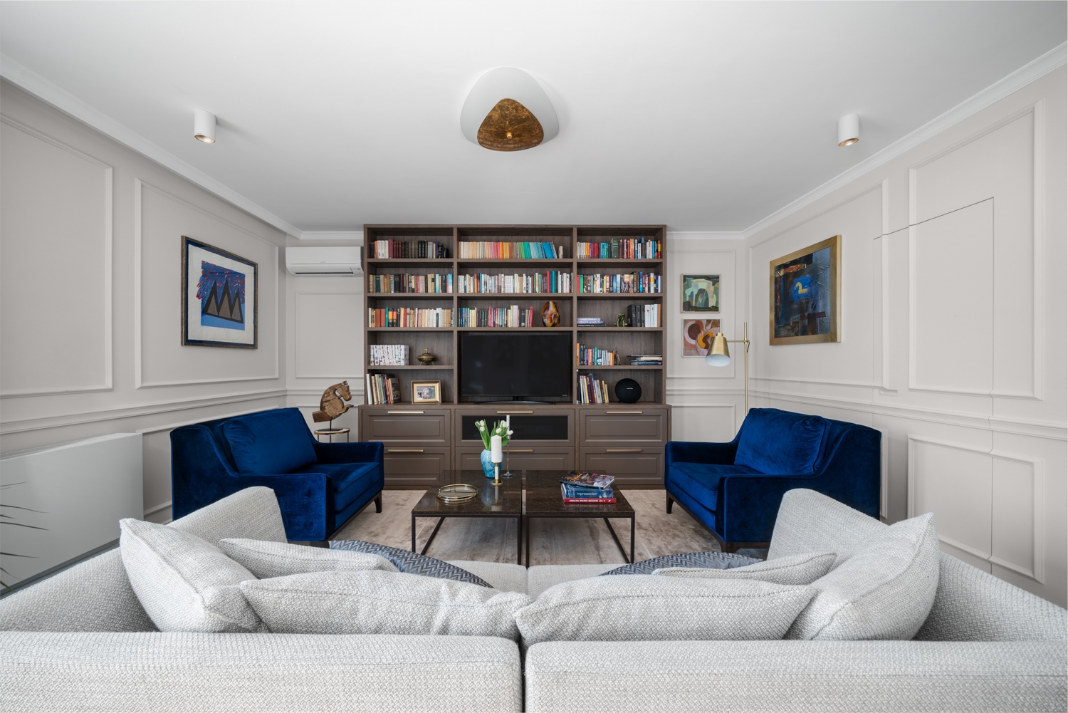 A szalonszerű nappali az időtlen klasszikus stílust képviseli elegáns bútoraival, egyedi, beépített könyvespolcával és kazettás falburkolatával, amelyben a rejtett ajtó egy praktikus tárolóba vezet.