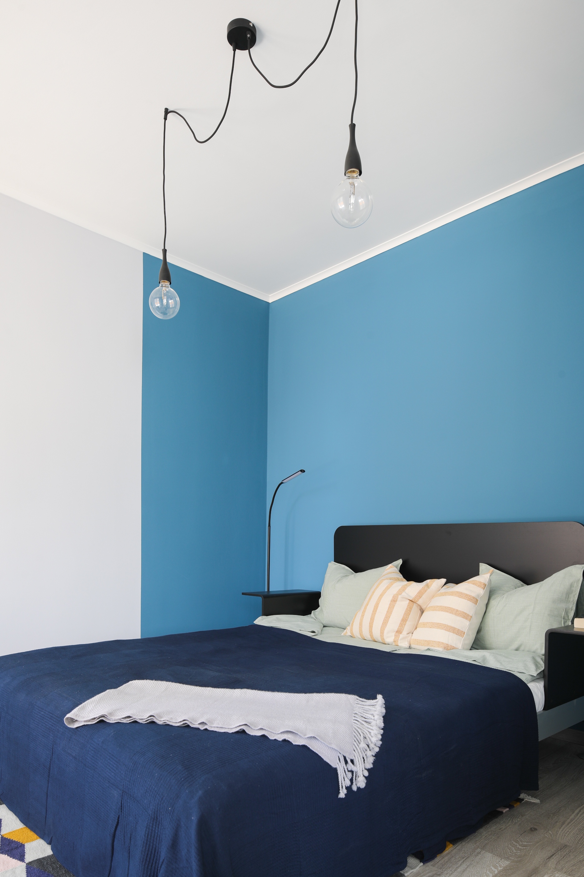 A sötétkék ágytakaróval higgadtabbá tett hálóban trükkös falfestés teszi még kuckósabbá a hangulatot – szintén a kék egy újabb árnyalatát vonultatva fel, ezúttal falfesték formájában.