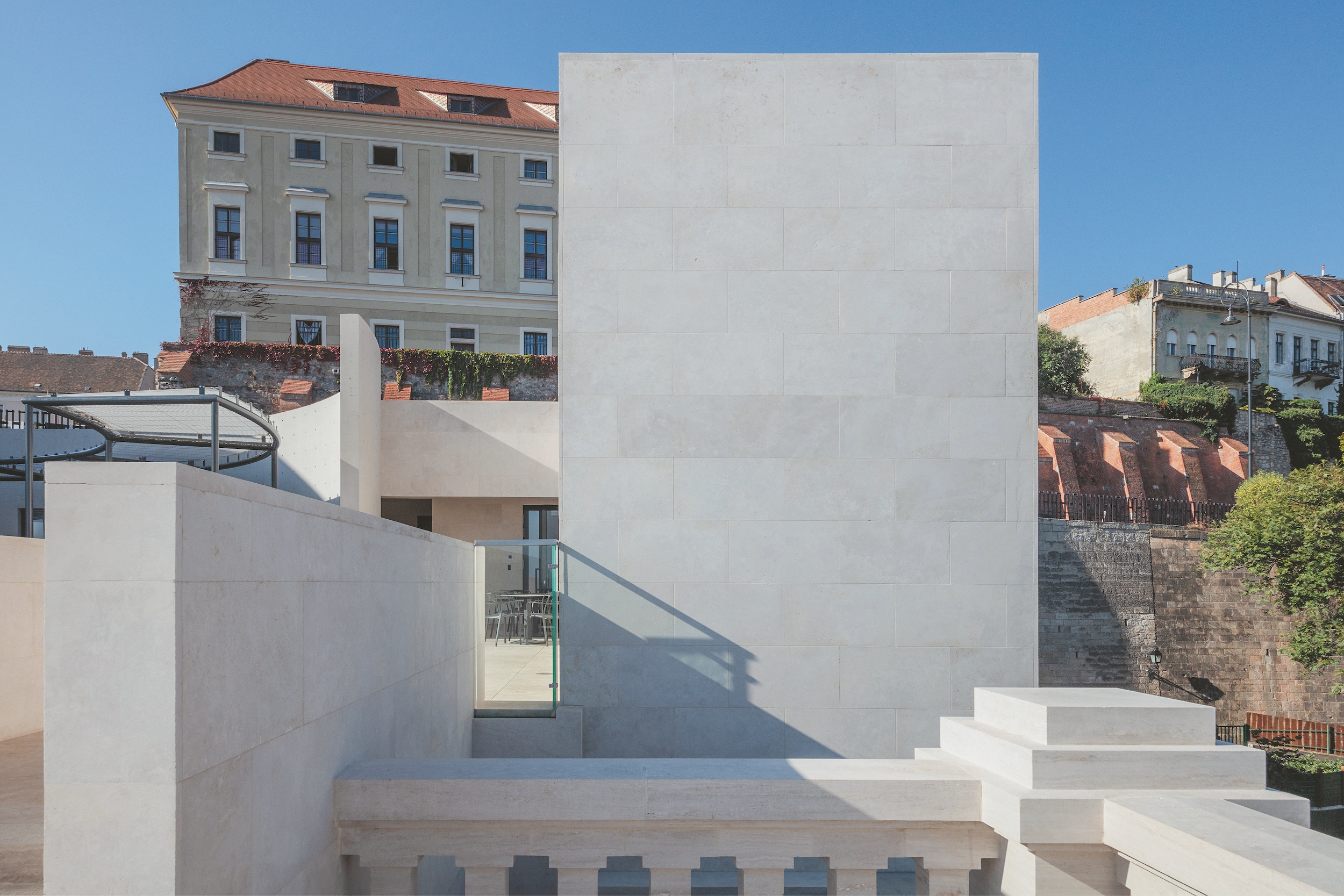 Az eredeti villaépület erős, karakteres ellenpontjaként hoz létre új térfalat az eredetileg művészrezidenciaként felépült minimalista épületszárny