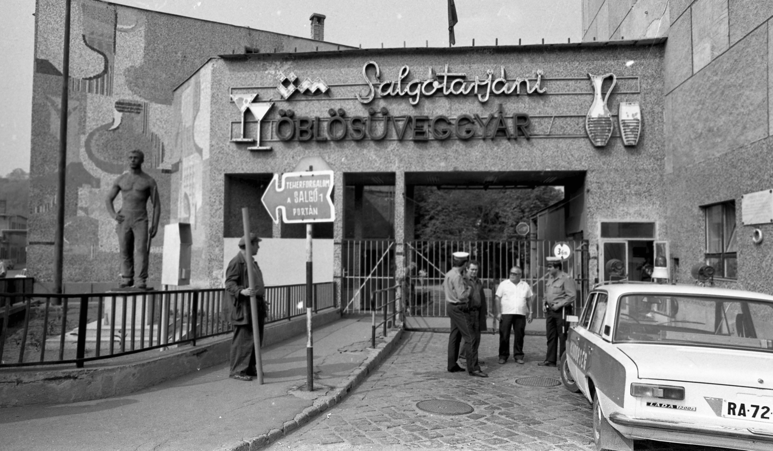 Salgótarján, Magyarország, 1982. A Salgótarjáni Öblösüveggyár bejárata a Rákóczi út felől, balra a Huta utca. Előtérben az Üvegfúvó című szobor (Ispánki József, 1961.), mögötte a falon Kanyák Zsófia üvegmozaikja (1972). Forrás: Fortepan / Magyar Rendőr