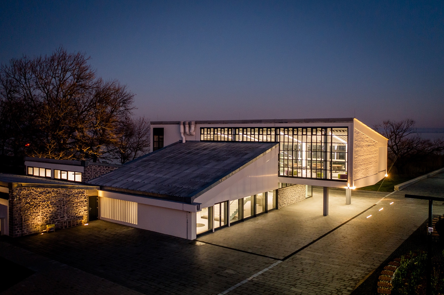 A hátsó üvegfalon feltűnik a régi, sűrű osztásrendszer, az alsó szinten pedig látszik az eredeti terveken is szereplő széles, nagyvonalú lépcső