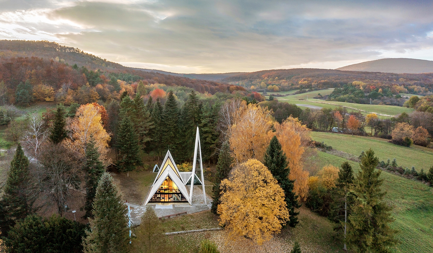 A fehérre meszelt falak, az árnyékban maradó, sötét elemek és az égbe nyúló hegyesszögek erőteljes látványt nyújtanak a lágy, lankás környezetben