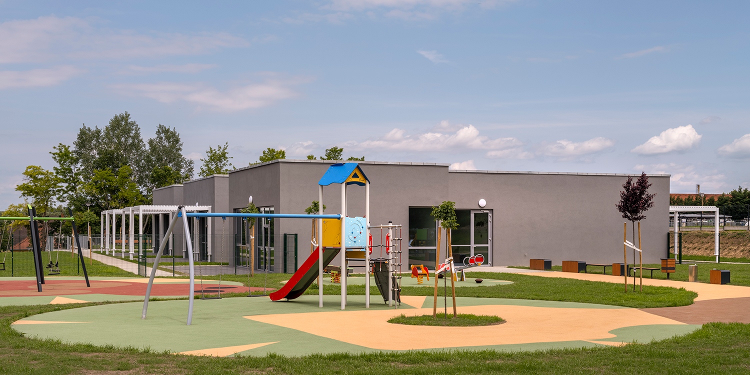 A gyermekek csoportszobái és játszóudvarai a telek belső, parkerdővel határos biztonságos környezetébe kerültek. A játszótér burkolatának formáját a környező természetben élő állatok ihlették.