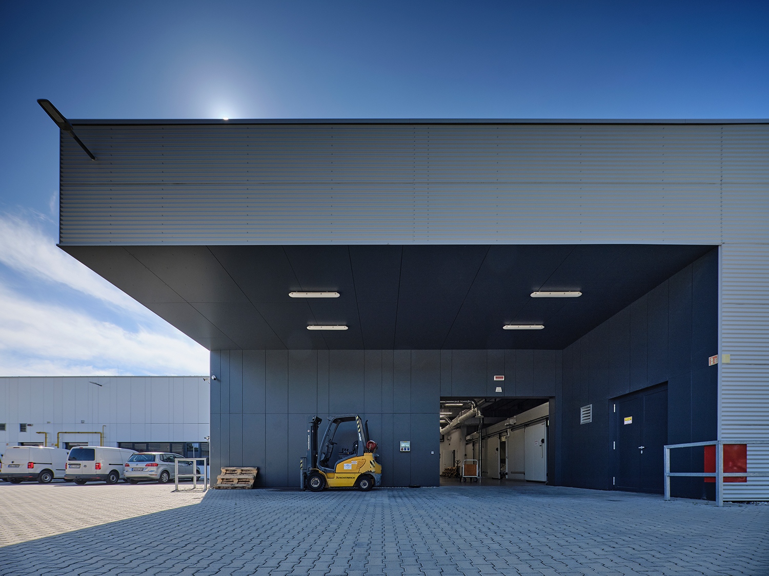 A kék, a szürke és a fehér látványos kombinációjával, valamint a lamellakiosztások ötletes variációival kialakított homlokzat-átmenetek egységes keretbe foglalják a kiegyensúlyozottságot sugárzó sokfunkciós épületegyüttest