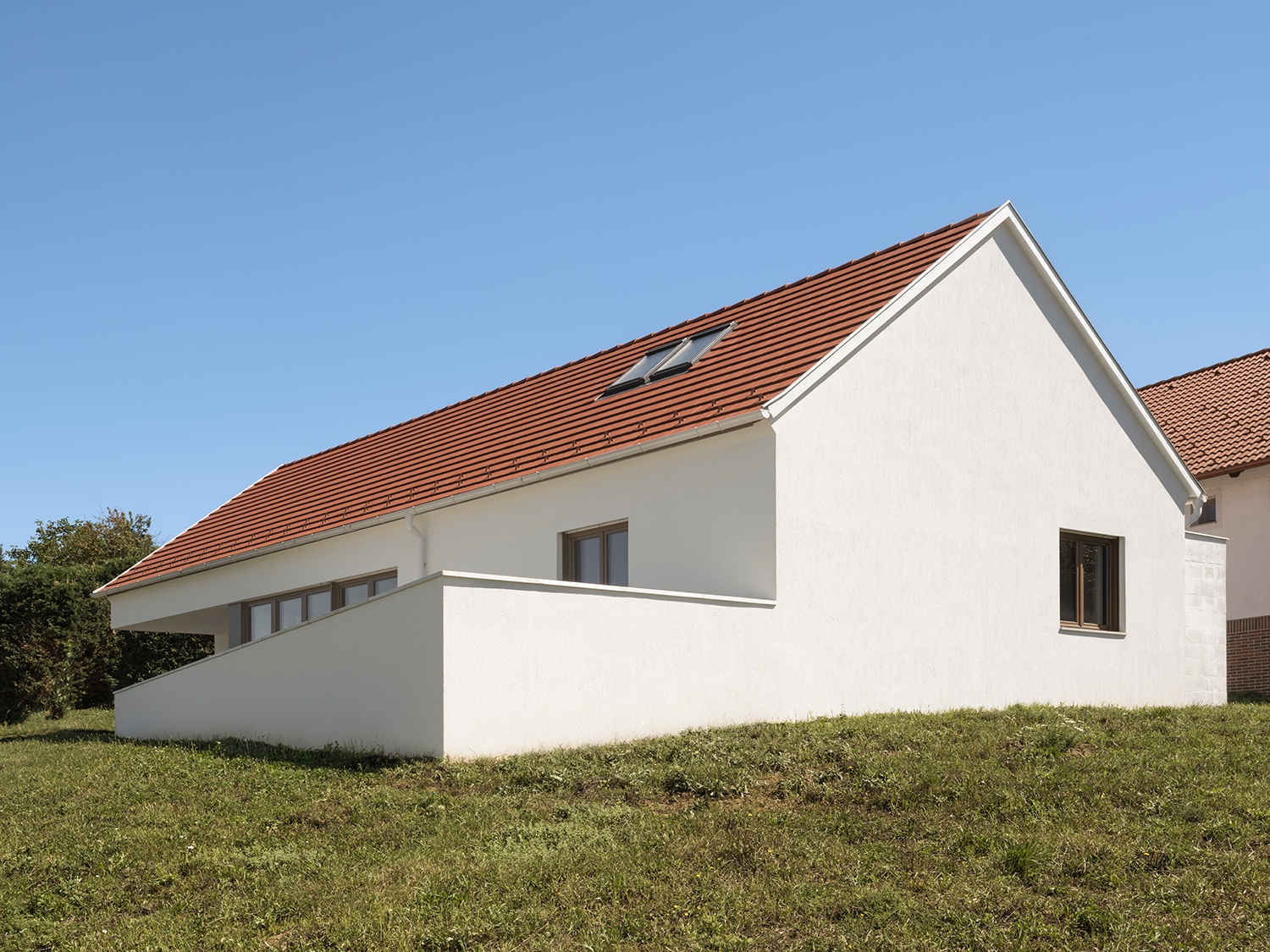 Az úttal körülölelt saroktelek-nyúlvány kerítés nélkülisége egyáltalán nem zavaró, hiszen a terasz falazata, illetve a garázs-átrium egység remekül határolja az épületet