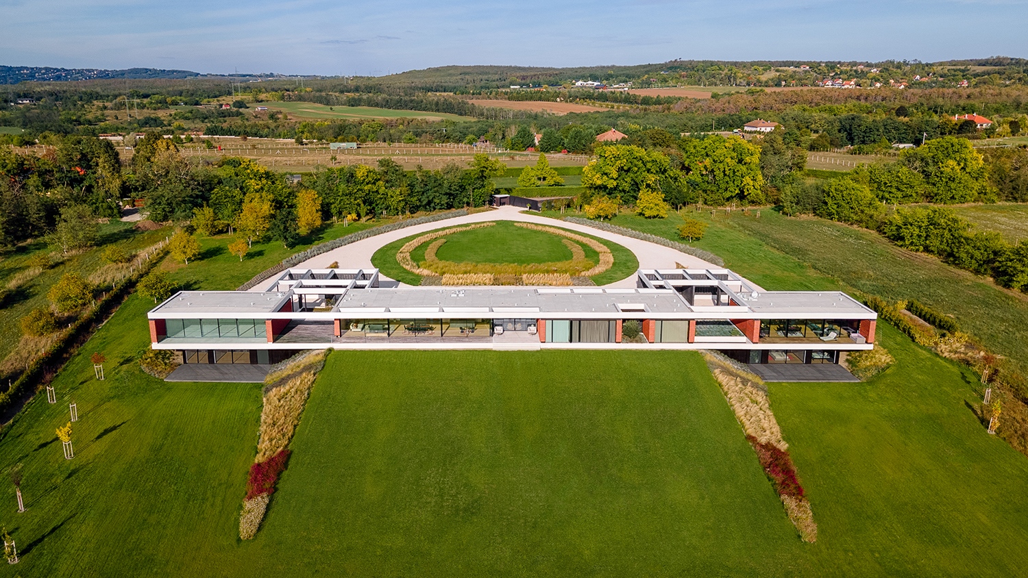 A generációk eltérő elképzeléseit a tervezőknek egy bravúrosan egyszerű megoldással sikerült összebékíteniük: az utca felől egyszintes ház alaplemezét kétoldalt konzolosan kinyújtották, és a kert irányából kétoldalt – a fiatalok lakásainál – alul egy plusz szinttel bővítették