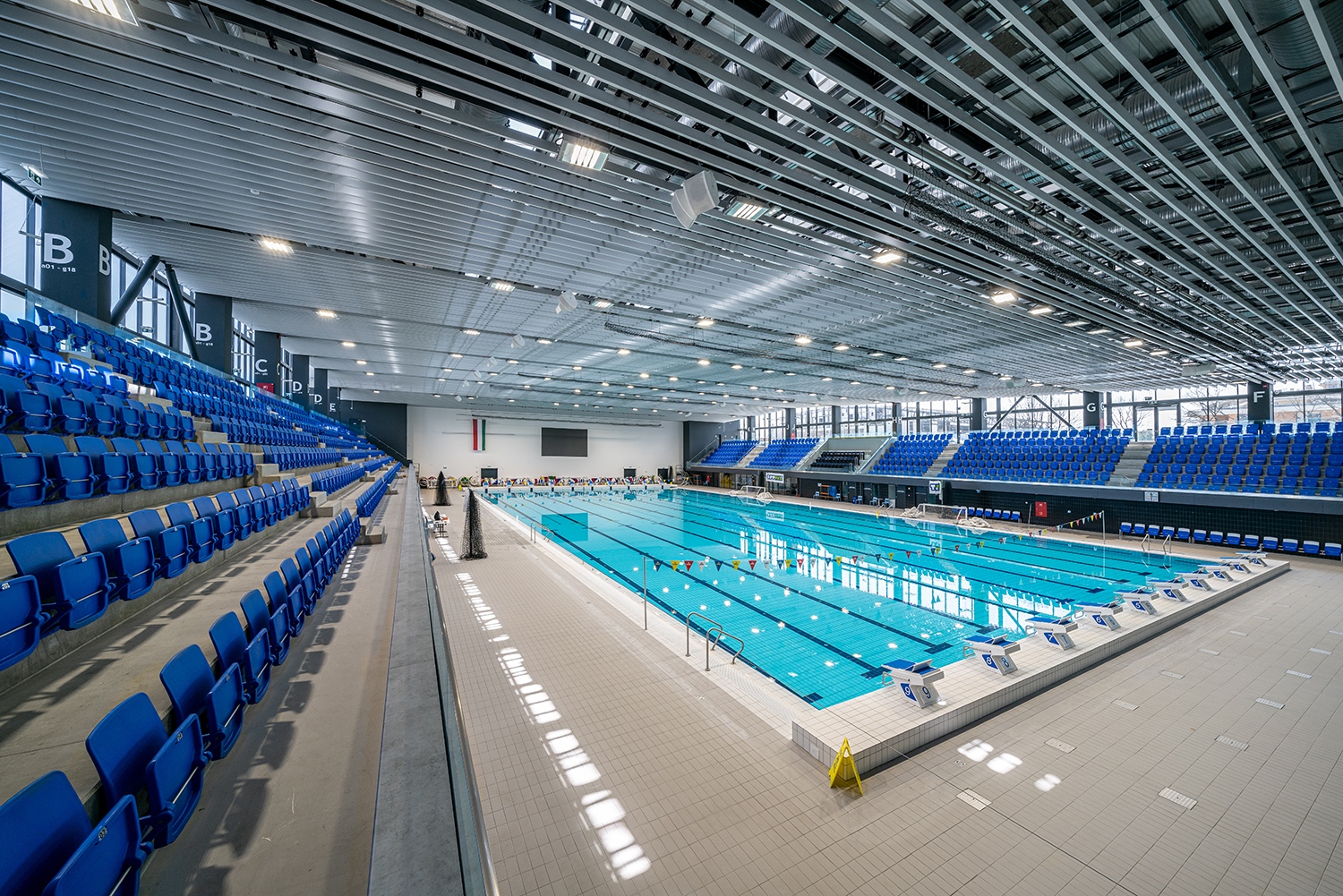 A medencetér fölé boruló, hol kissé megemelkedő, hol lehajló, fémbordákból kialakított álmennyezet nem takarja el teljesen a fölötte húzódó gépészetet, de leveszi a látványról annak részleteit